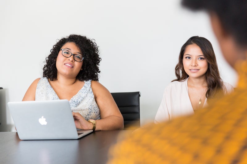 Group of Black women in a professional boardroom meeting with laptops and presentation screen