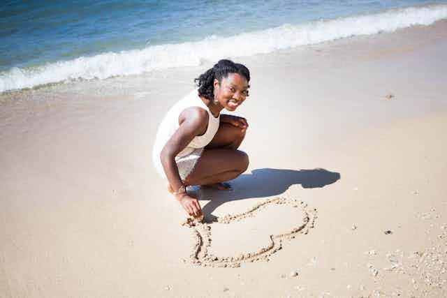 Woman smiling into camera drawing on sand