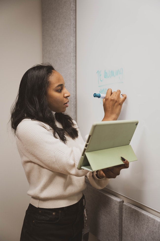 Focused Woman Writing on Whiteboard with Tablet